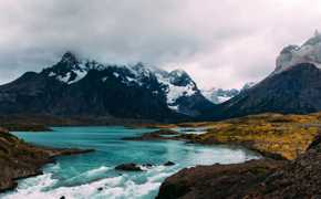 Turquoise glacial waters reflect rugged, snow-capped peaks beneath a moody sky in Torres del Paine National Park, Chile. 