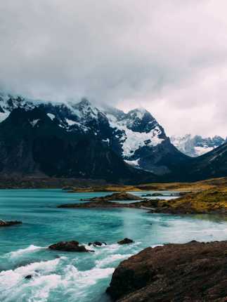 Turquoise glacial waters reflect rugged, snow-capped peaks beneath a moody sky in Torres del Paine National Park, Chile. 