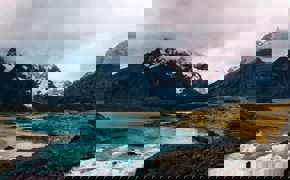 Turquoise glacial waters reflect rugged, snow-capped peaks beneath a moody sky in Torres del Paine National Park, Chile. 