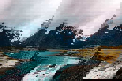 Turquoise glacial waters reflect rugged, snow-capped peaks beneath a moody sky in Torres del Paine National Park, Chile. 