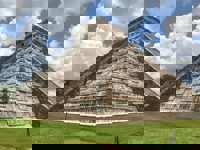 Temple of Kukulcan pyramid at Chichen Itza, Yucatan, Mexico, with cloudy blue sky and green grass foreground. 