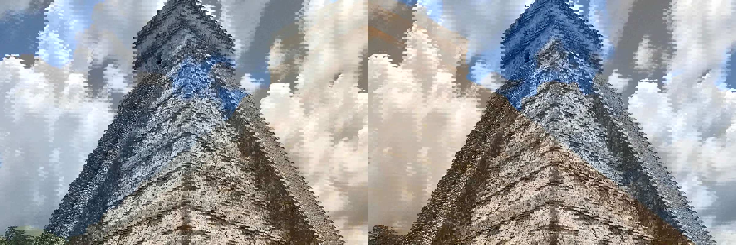 Temple of Kukulcan pyramid at Chichen Itza, Yucatan, Mexico, with cloudy blue sky and green grass foreground. 