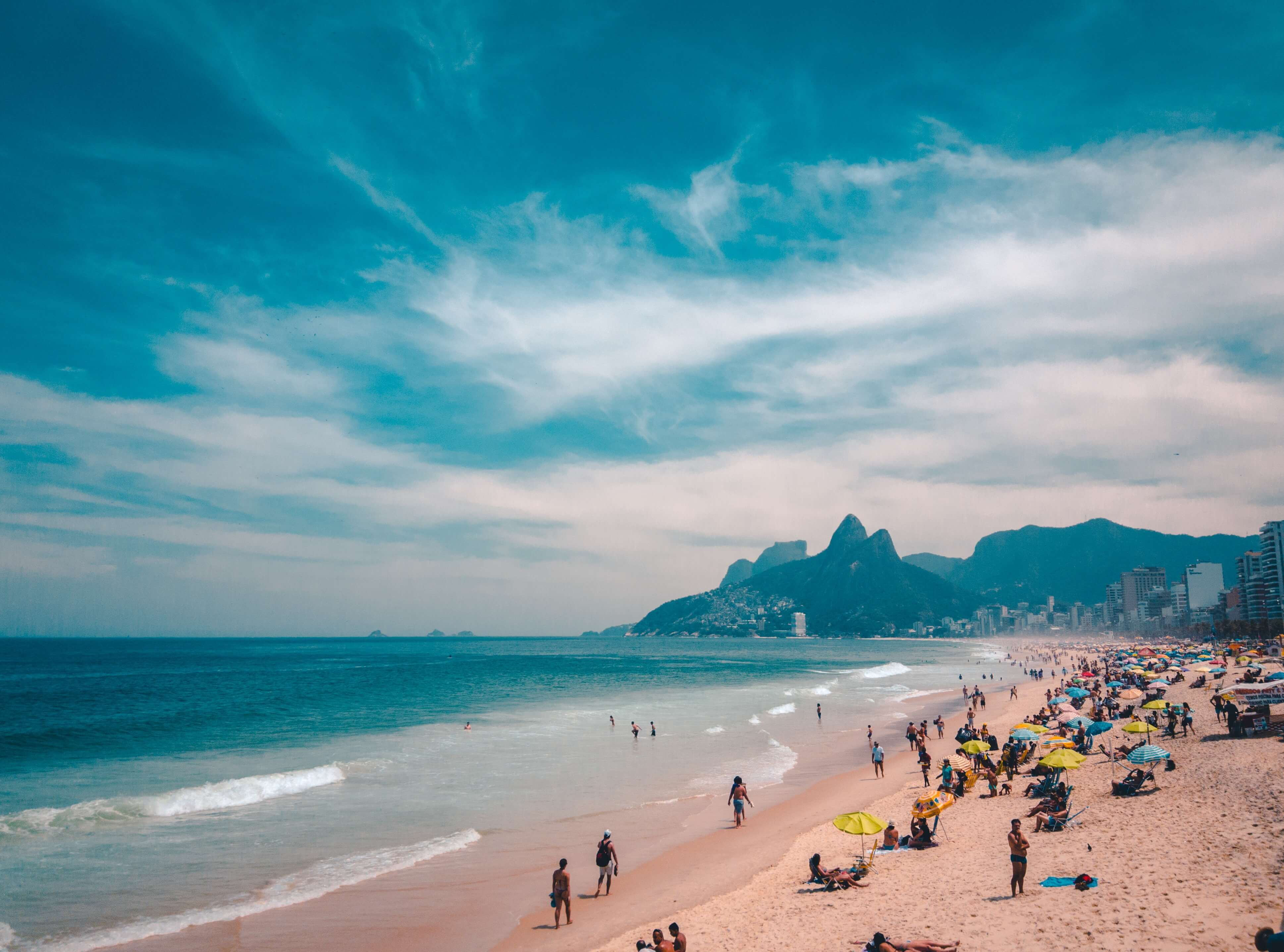 View of Ipanema Beach with beachgoers, ocean waves, and the Two Brothers Mountain in Rio de Janeiro, Brazil. 