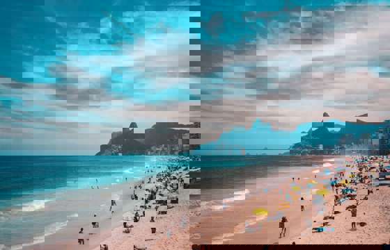 View of Ipanema Beach with beachgoers, ocean waves, and the Two Brothers Mountain in Rio de Janeiro, Brazil. 
