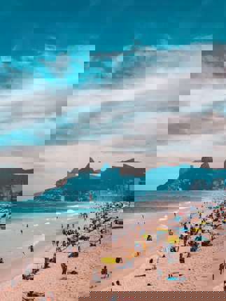 View of Ipanema Beach with beachgoers, ocean waves, and the Two Brothers Mountain in Rio de Janeiro, Brazil. 