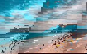 View of Ipanema Beach with beachgoers, ocean waves, and the Two Brothers Mountain in Rio de Janeiro, Brazil.