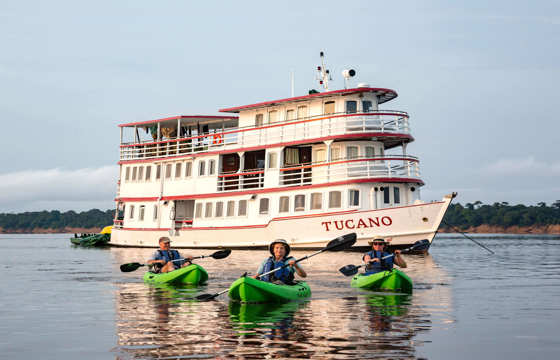 Guests kayaking on the Amazon River with the Tucano expedition cruise boat in the background.