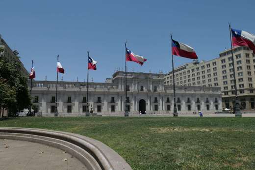 La Moneda Palace in Santiago, Chile framed by waving national flags on a clear day in the capital's civic center. 