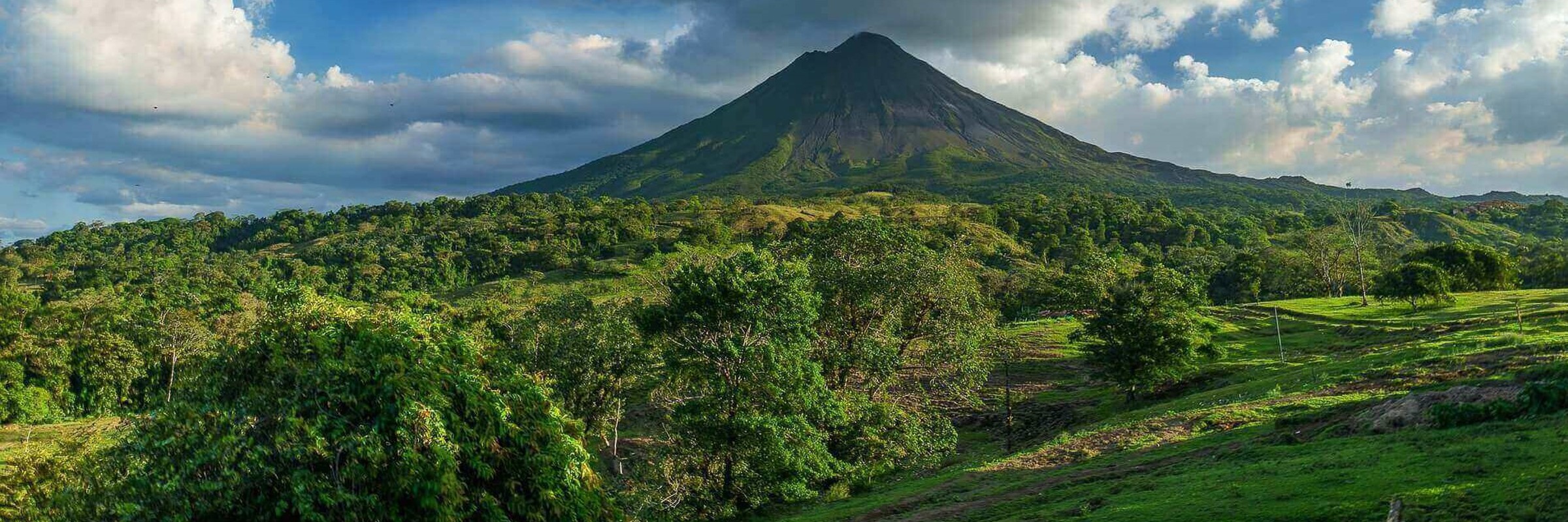 Central America - Costa Rica, lush greenery surrounding the majestic Arenal Volcano under a bright blue sky. 