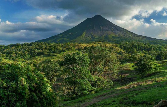 Central America - Costa Rica, lush greenery surrounding the majestic Arenal Volcano under a bright blue sky.