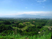 A panoramic view of San Jose and Alajuela with scattered homes and lush greenery set against misty central mountains.