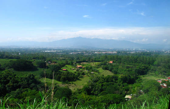 A panoramic view of San Jose and Alajuela with scattered homes and lush greenery set against misty central mountains.
