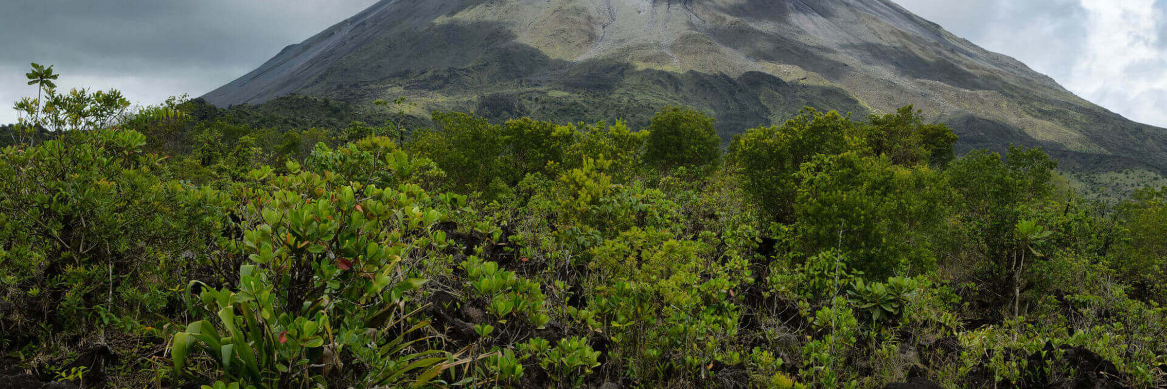 A scenic view of Arenal Volcano rising above lush green forest in Arenal National Park, Costa Rica. 