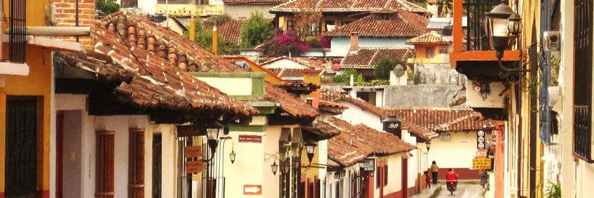 Cobbled street in San Cristobal de las Casas, Mexico, with colonial buildings, colourful facades, and locals walking. 