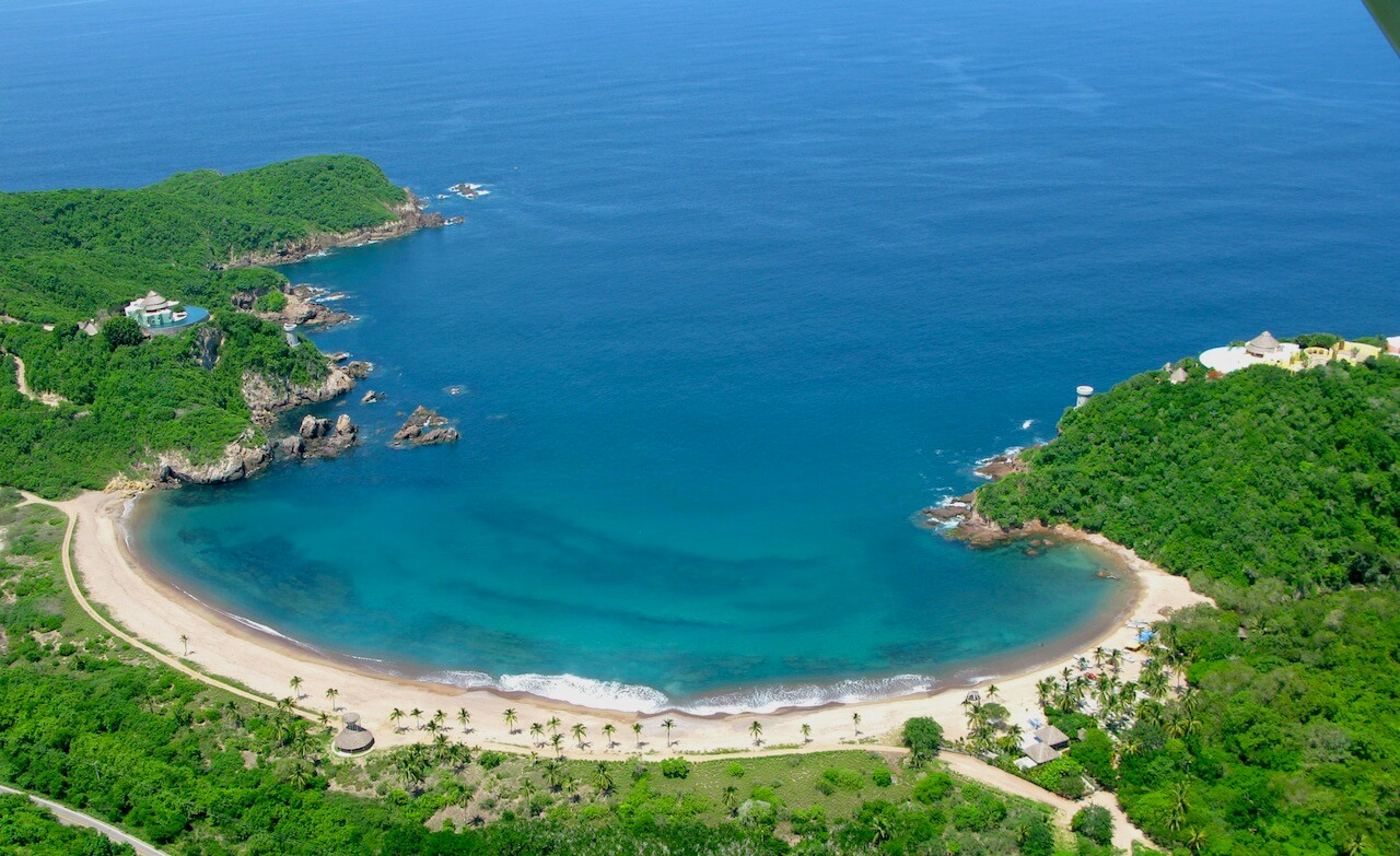Aerial view of Costa Careyes, showcasing a secluded crescent-shaped beach and lush greenery along Mexico's Pacific Coast. 