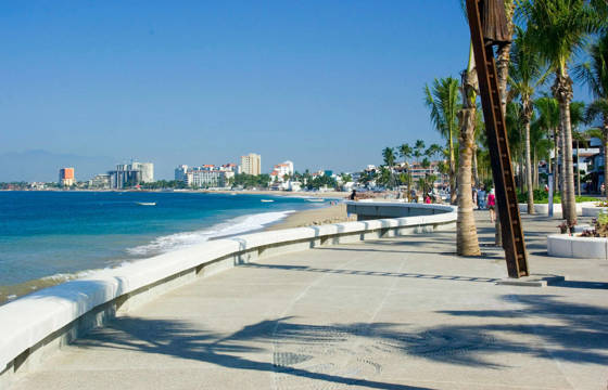 View of the Malecon promenade in Puerto Vallarta, Mexico, lined with palm trees, sculptures, and Pacific coastline views. 
