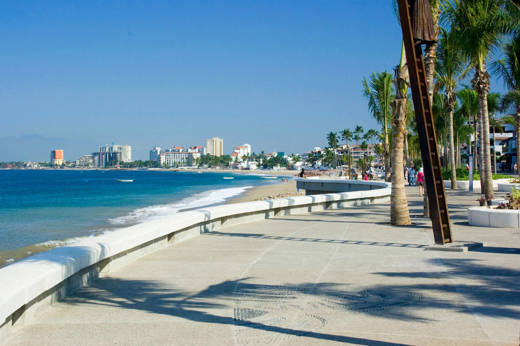 View of the Malecon promenade in Puerto Vallarta, Mexico, lined with palm trees, sculptures, and Pacific coastline views. 