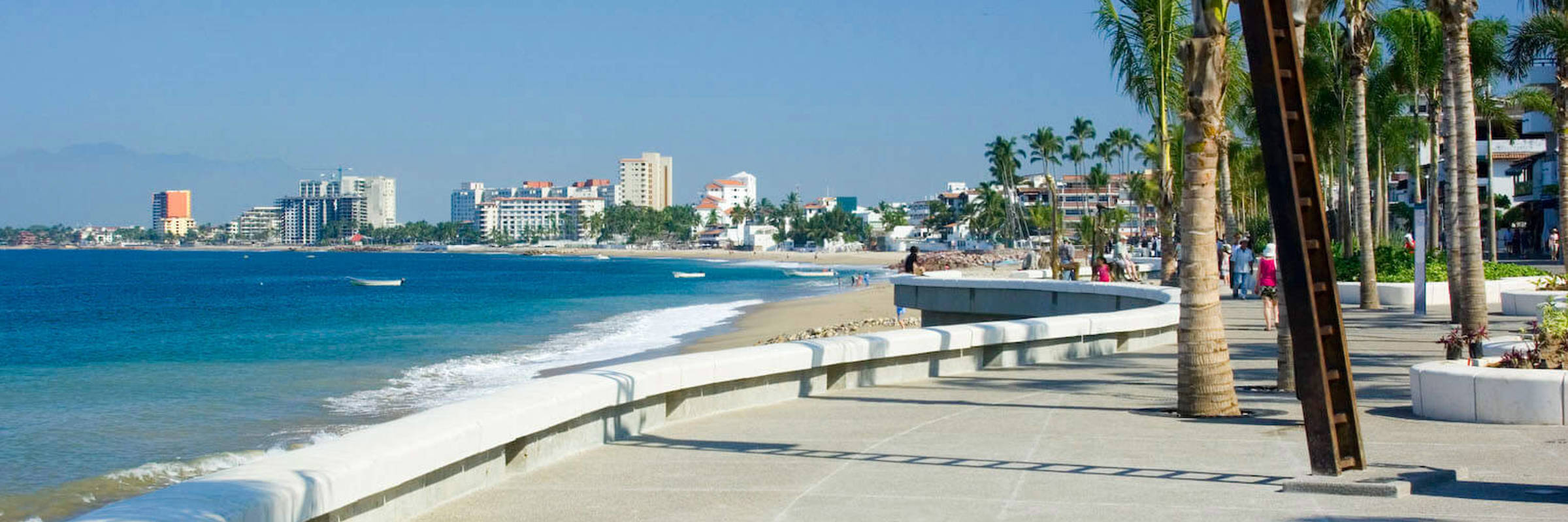 View of the Malecon promenade in Puerto Vallarta, Mexico, lined with palm trees, sculptures, and Pacific coastline views. 