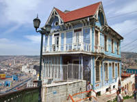 A traditional blue wooden house with ornate trim overlooks the hills and coast of Valparaiso, Chile.
