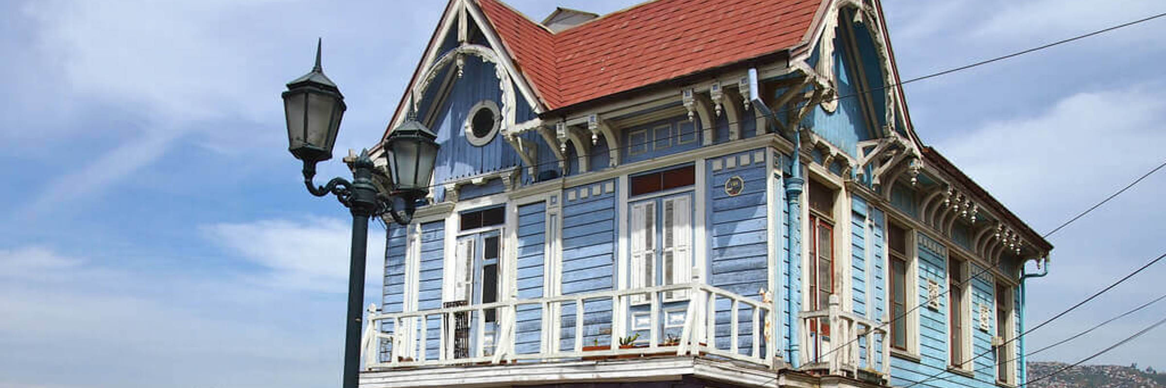 A traditional blue wooden house with ornate trim overlooks the hills and coast of Valparaiso, Chile.