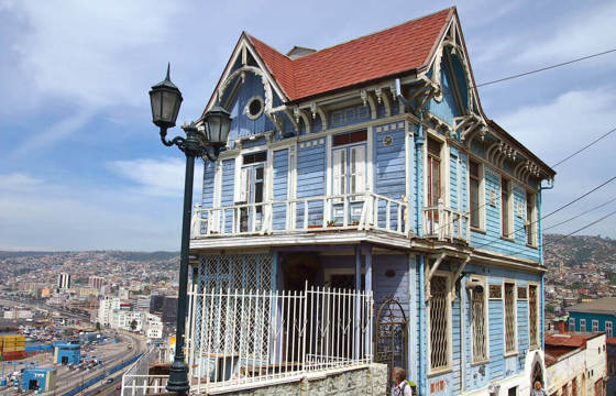 A traditional blue wooden house with ornate trim overlooks the hills and coast of Valparaiso, Chile.