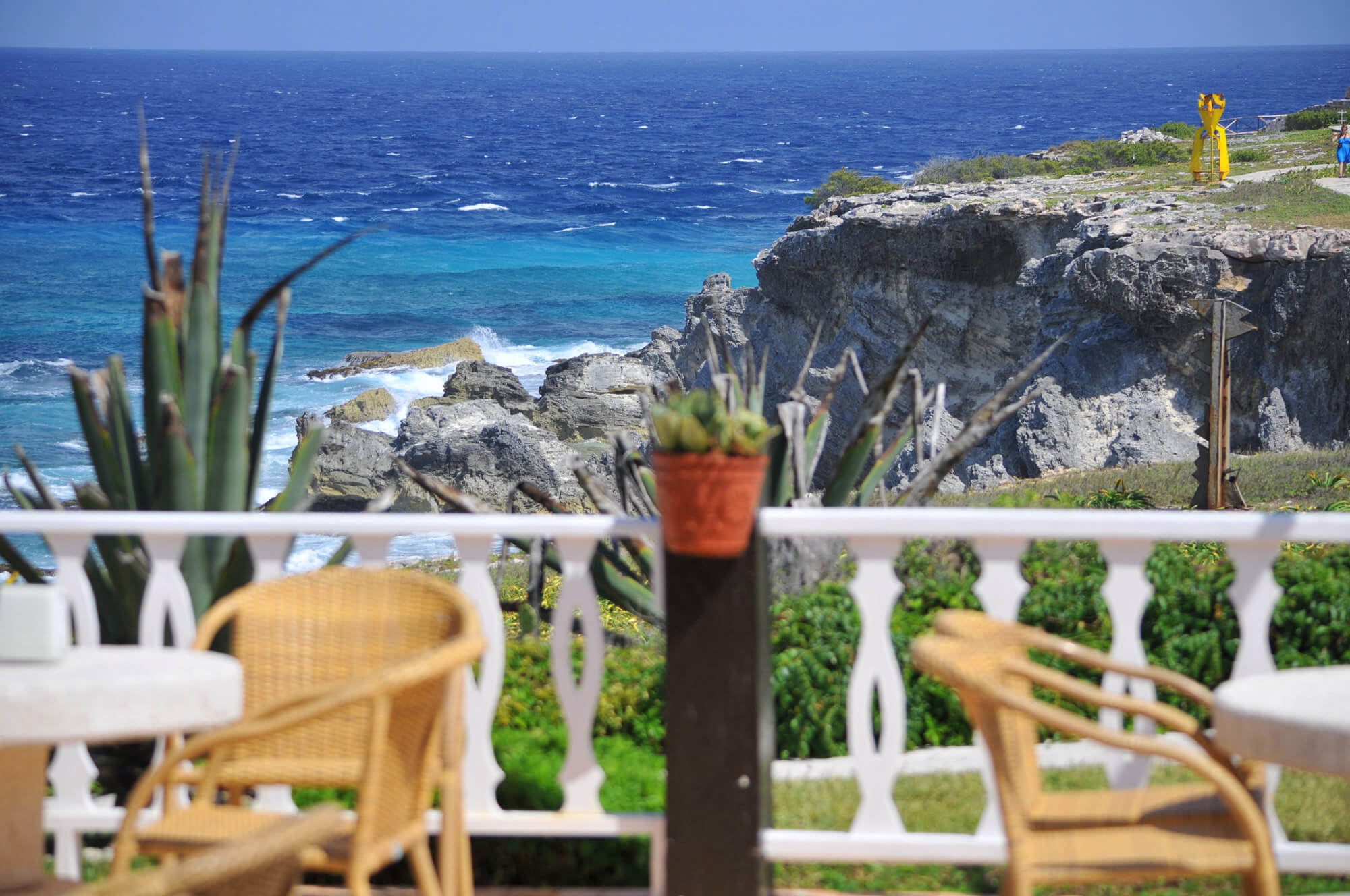 Scenic ocean view from a restaurant terrace on Isla Mujeres white fence, chairs, rocky cliffs, and turquoise Caribbean sea. 