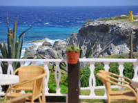 Scenic ocean view from a restaurant terrace on Isla Mujeres white fence, chairs, rocky cliffs, and turquoise Caribbean sea. 