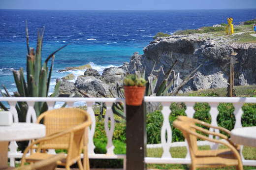 Scenic ocean view from a restaurant terrace on Isla Mujeres white fence, chairs, rocky cliffs, and turquoise Caribbean sea. 