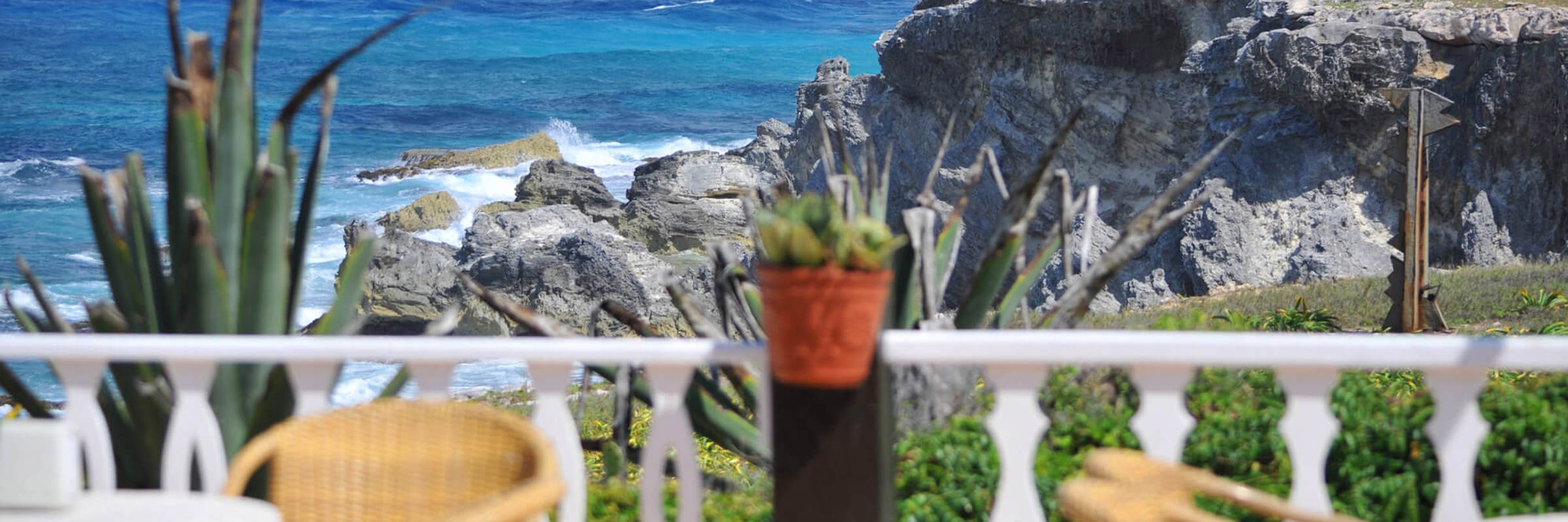 Scenic ocean view from a restaurant terrace on Isla Mujeres white fence, chairs, rocky cliffs, and turquoise Caribbean sea. 