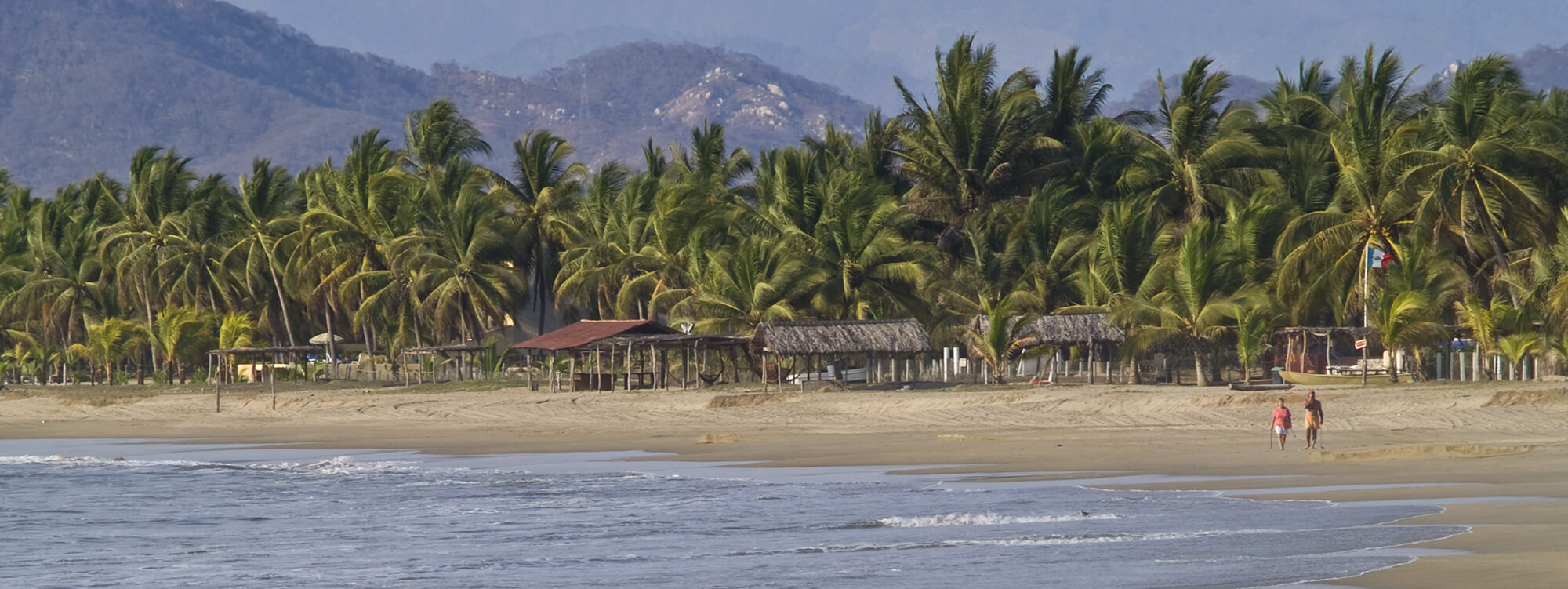 Scenic beach view with palm trees and distant hills at Zihuatanejo, a laid-back fishing village on Mexico's Pacific Coast. 