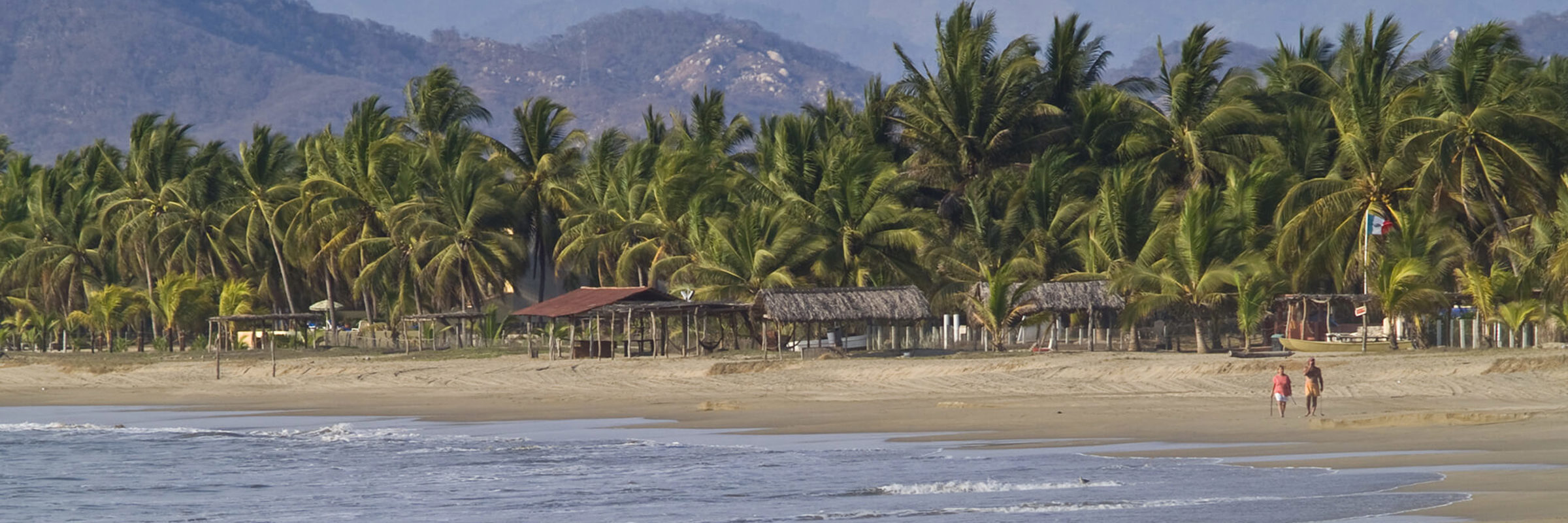 Scenic beach view with palm trees and distant hills at Zihuatanejo, a laid-back fishing village on Mexico's Pacific Coast. 