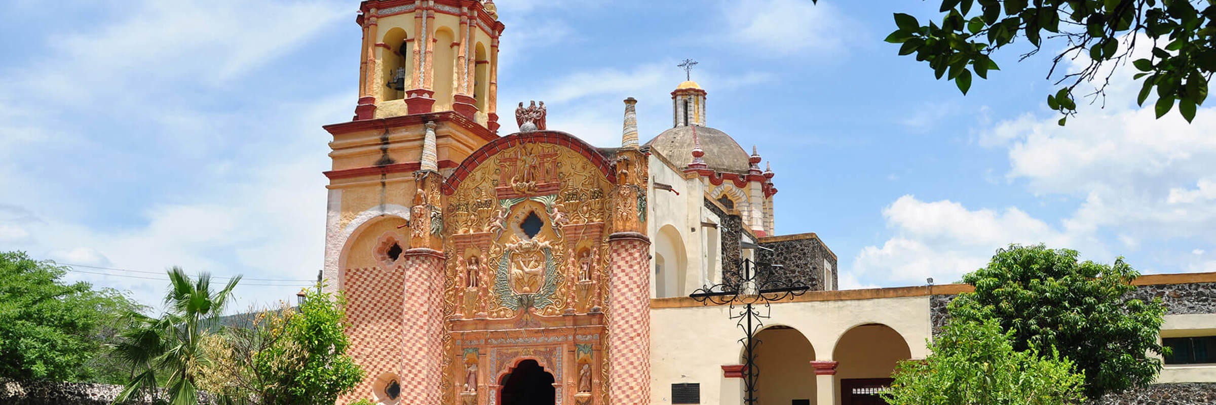 Colonial red-brick church in Queretaro, Mexico, surrounded by trees and blue sky, showcasing local architecture. 