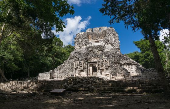 The main temple at Chicanna archaeological site, surrounded by jungle, featuring intricate Maya stucco decorations. 