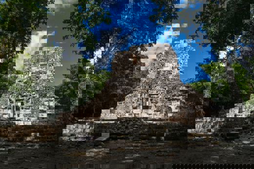 The main temple at Chicanna archaeological site, surrounded by jungle, featuring intricate Maya stucco decorations. 