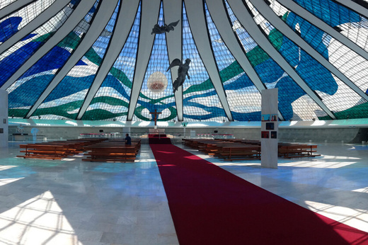 Interior of the Cathedral of Brasilia, showcasing stained glass ceiling and suspended angel sculptures in modernist design. 