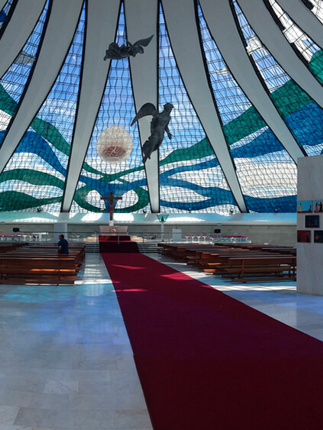 Interior of the Cathedral of Brasilia, showcasing stained glass ceiling and suspended angel sculptures in modernist design. 