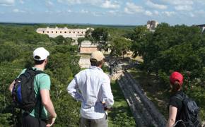 Tourists enjoying a panoramic view of the ancient Mayan ruins at Uxmal, Yucatan, Mexico, surrounded by dense green jungle. 