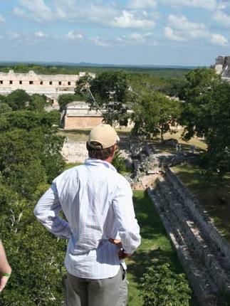Tourists enjoying a panoramic view of the ancient Mayan ruins at Uxmal, Yucatan, Mexico, surrounded by dense green jungle. 