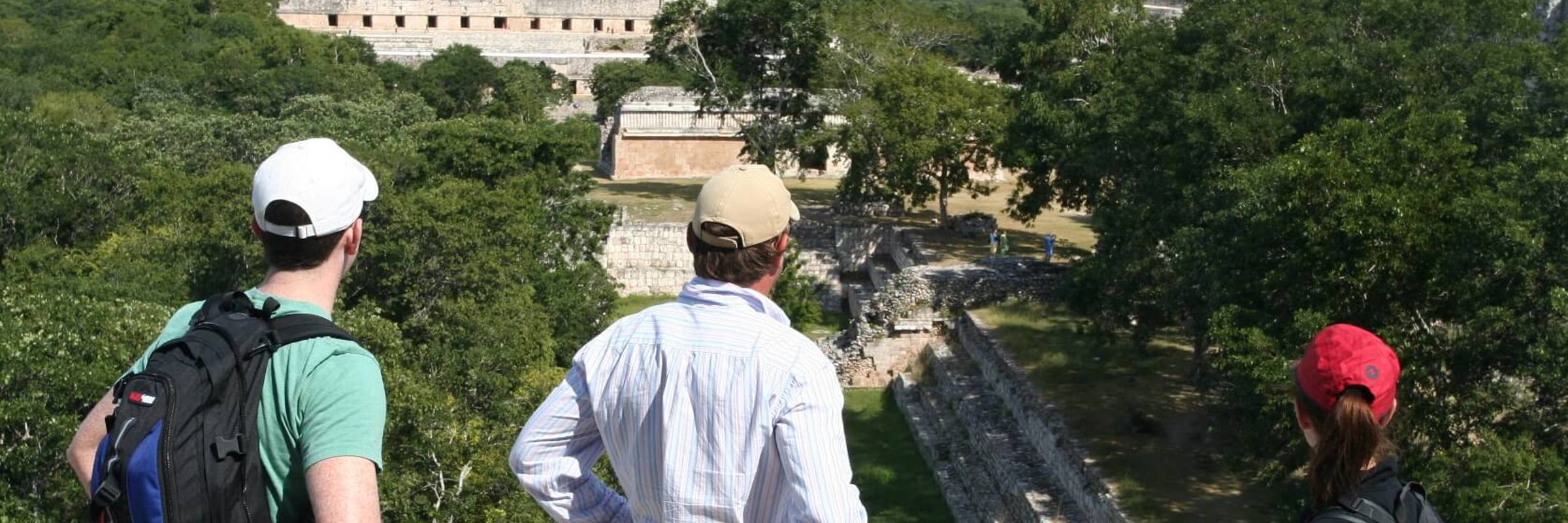 Tourists enjoying a panoramic view of the ancient Mayan ruins at Uxmal, Yucatan, Mexico, surrounded by dense green jungle. 