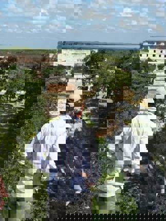 Tourists enjoying a panoramic view of the ancient Mayan ruins at Uxmal, Yucatan, Mexico, surrounded by dense green jungle. 