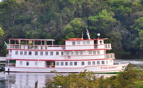 The Tucano Amazon cruise boat on the Rio Negro surrounded by lush rainforest, near Manaus, Brazil.