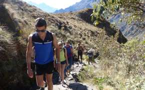 A family hikes together along a rugged mountain trail, immersed in Peru's Sacred Valley landscape. 