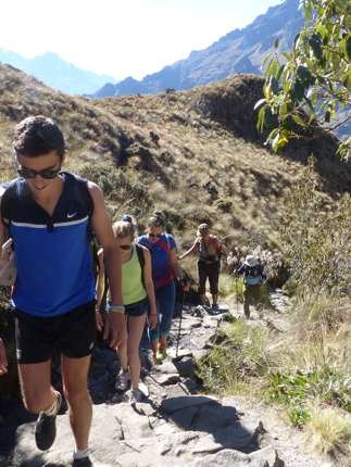A family hikes together along a rugged mountain trail, immersed in Peru's Sacred Valley landscape. 