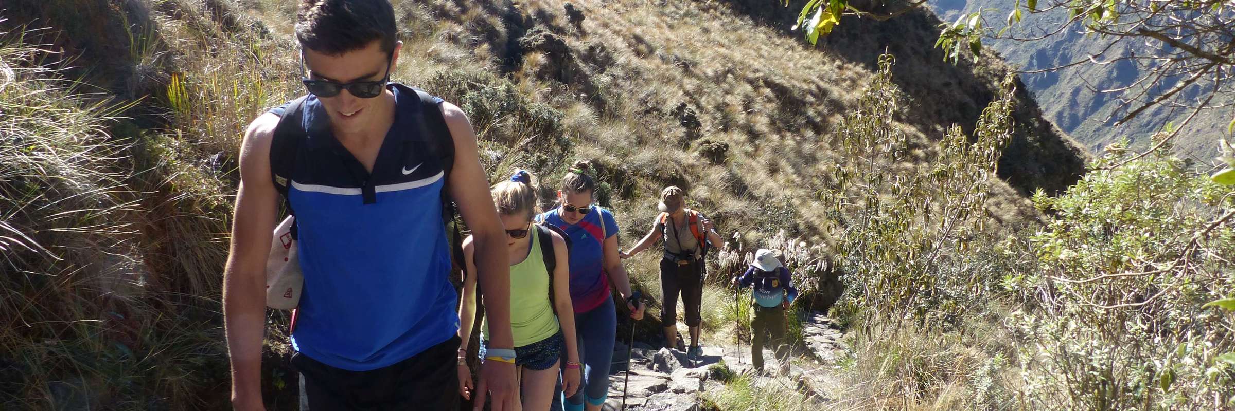 A family hikes together along a rugged mountain trail, immersed in Peru's Sacred Valley landscape. 