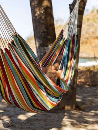 Relaxing in a colourful hammock strung between palm trees on a quiet tropical beach. 