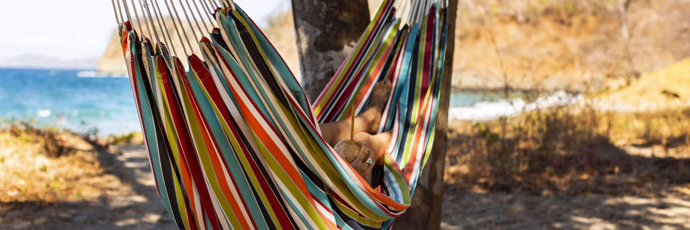 Relaxing in a colourful hammock strung between palm trees on a quiet tropical beach. 