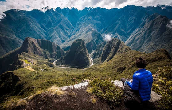 Hiker overlooking the Machu Picchu ruins from a high mountain viewpoint in the Peruvian Andes.