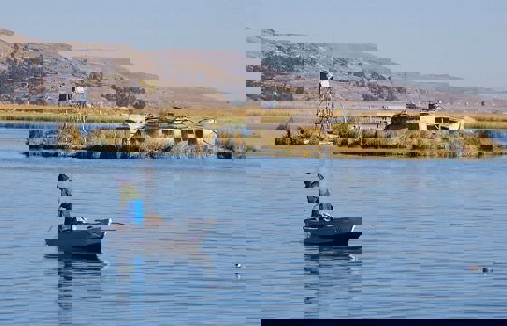 A local fisherman rows past reed islands on the tranquil blue waters of Lake Titicaca.