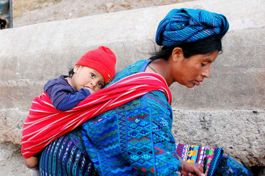 Central America - Guatemala, Indigenous mother carries child in traditional woven clothing, reflecting daily life and culture. 