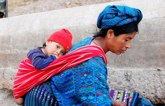 Central America - Guatemala, Indigenous mother carries child in traditional woven clothing, reflecting daily life and culture.